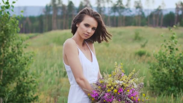 Una mujer joven de pie en el campo verde con ramo de flores — Vídeo de stock