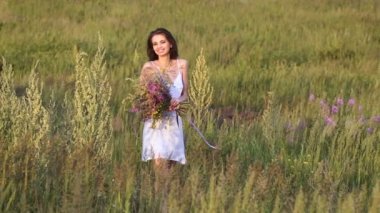 Çiçek demeti ile yeşil alanda yürüyen ve gülümseyen genç bir kadın