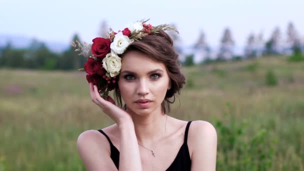 Vacker flicka i svart kort klänning med kransen på huvudet på det gröna fältet. — Stockvideo