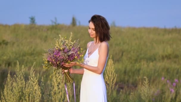 One young woman standing on green field smelling flower bunch — Stock Video