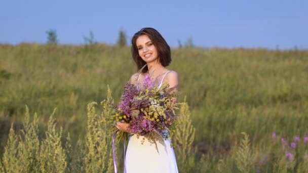 Одна молодая женщина стоит на зеленом поле с цветочным пучком и улыбается — стоковое видео