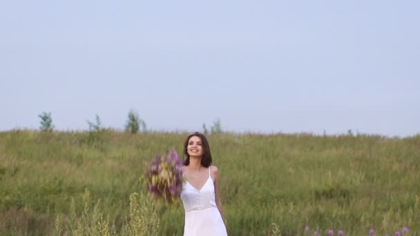 En ung kvinna stående på gröna fältet kastar en blomma gäng — Stockvideo