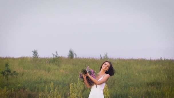 Одна молода жінка стоїть на зеленому полі кидає букет квітів — стокове відео