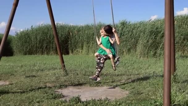 Schöne junge Frau mit einem charmanten kleinen Mädchen, das im Freien schwingt — Stockvideo