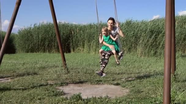 Beautiful young woman with a charming little girl swinging outdoors — Stock Video