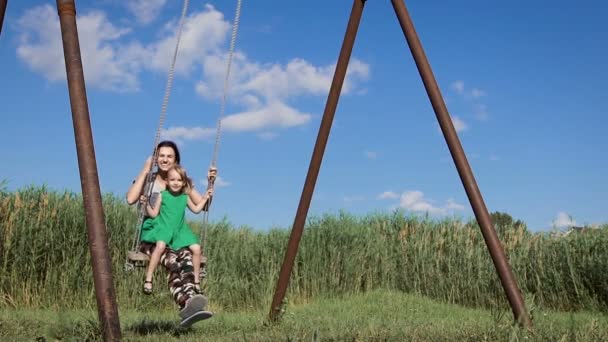 Beautiful young woman with a charming little girl swinging outdoors — Stock Video