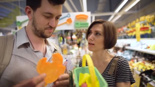 Hermosa pareja joven eligiendo en la tienda juguetes para niños — Vídeo de stock