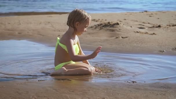 Söt liten blond flicka spelar med sand på en sjö — Stockvideo