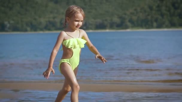 Menina loira bonito correndo por um lago com as montanhas verdes no fundo — Vídeo de Stock