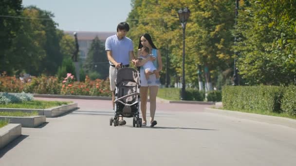 Joven familia caminando por el parque de la ciudad con un niño en sus brazos . — Vídeo de stock