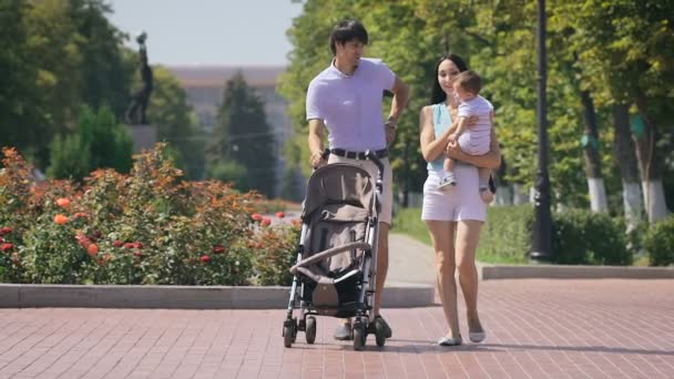 Keluarga muda berjalan di taman kota dengan seorang anak kecil dalam pelukannya . — Stok Video