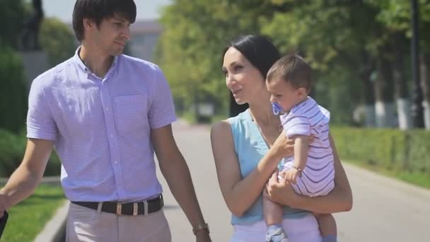 Giovane famiglia che cammina sul parco della città con un bambino tra le braccia . — Video Stock