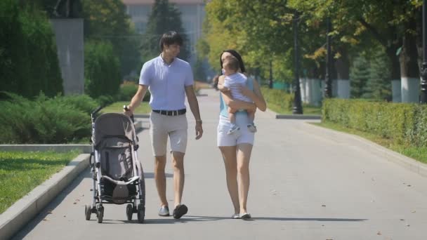 Junge Familie spaziert mit kleinem Jungen auf dem Arm durch den Stadtpark. — Stockvideo