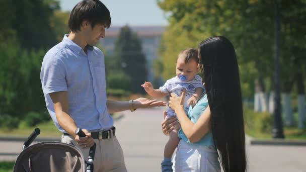 Jovem família caminhando no parque da cidade com um menino em seus braços . — Vídeo de Stock