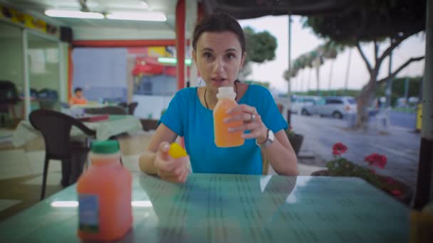 Woman drinking glass of orange juice sitting at a restaurant — Stock Video