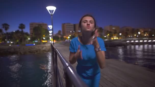 Una hermosa mujer bailando cerca del mar y mirando el panorama nocturno de la ciudad — Vídeo de stock