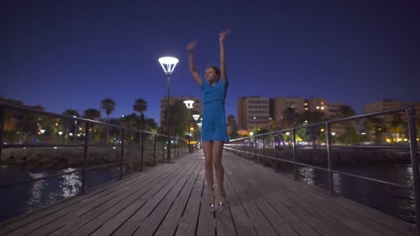 Een mooie vrouw springen in de buurt van de zee en kijken naar nacht stad panorama — Stockvideo