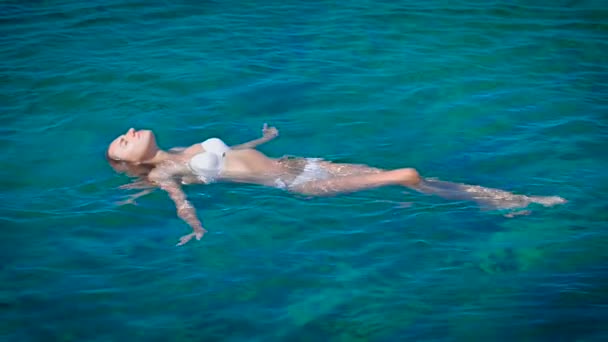 Μια ευτυχισμένη γυναίκα στο λευκό μπικίνι κολύμβηση στο γαλάζιο της θάλασσας — Αρχείο Βίντεο