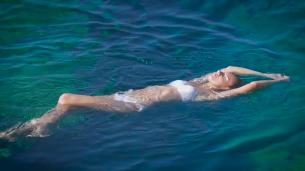 Молодая счастливая женщина в белом бикини плавает в лазурном море — стоковое видео