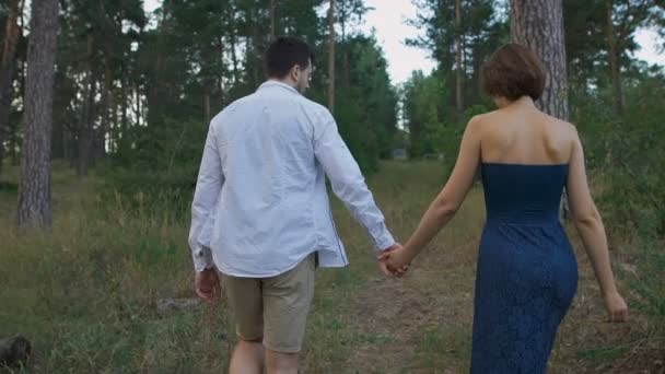 Un hombre agradable con barba lleva a su hermosa esposa o niña por un sendero en el bosque . — Vídeos de Stock