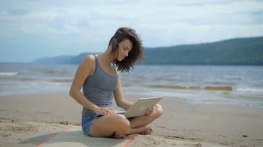 Güzel seksi genç Inspirated Bayan dizüstü bilgisayar kullanarak bir kumsalda oturuyor