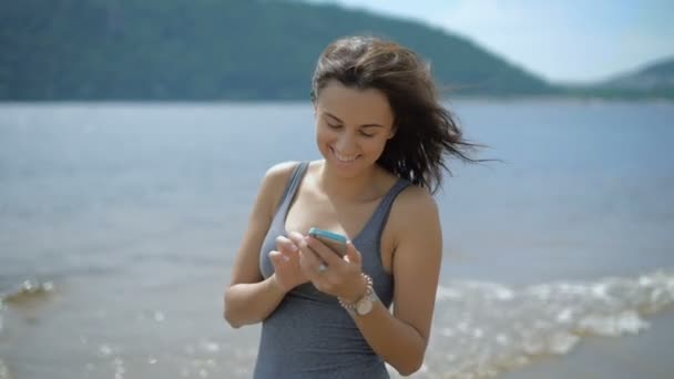 En ung vacker kvinna chattar med en vän på en strand — Stockvideo