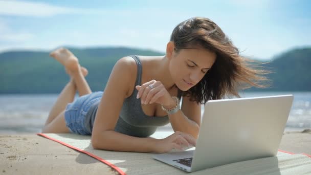 Красивая сексуальная молодая расслабленная леди лежит на своем Томми на пляже с помощью ноутбука — стоковое видео