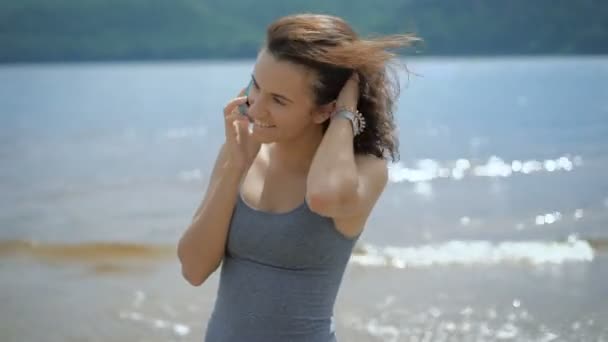 Una joven hermosa mujer hablando con su novio usando un teléfono inteligente en una playa — Vídeo de stock