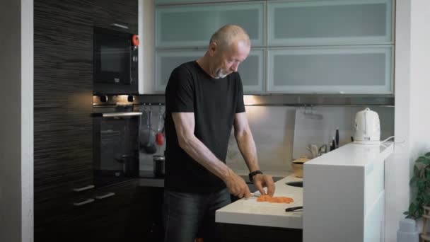 Mannen vid en ålder som förbereder en måltid i deras moderna kök. — Stockvideo