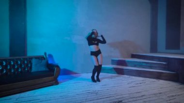 Siyah kısa elbiseli sarışın stüdyoda dans ediyor. Bir kadın modern dinamik bir dans sergiliyor..