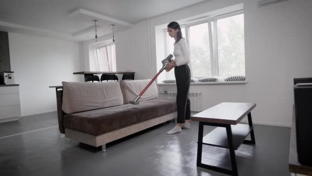 Een moderne draadloze stofzuiger. Handmatig reinigen in een grote woonkamer, brunette meisje. — Stockvideo