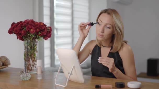 Mooie jonge vrouw brengt make-up aan. De blonde schildert haar gezicht om er beter uit te zien. — Stockvideo