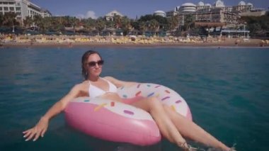 Bekini 'de güzel bir kadın denizde dinleniyor. Güneş gözlüklü genç bir kadın şişirilebilir bir dairede yüzüyor..