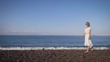 Akdeniz 'in arka planında narin genç bir kadın. Bir yaz günü kıyı şeridinde yürümek.