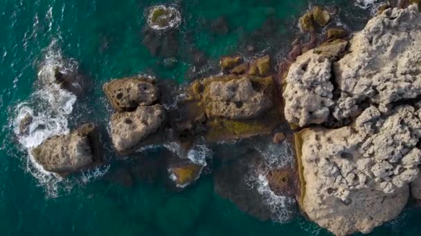 Vista aerea. Costa rocciosa e mare azzurro. Onde si schiantano contro grandi rocce. — Video Stock