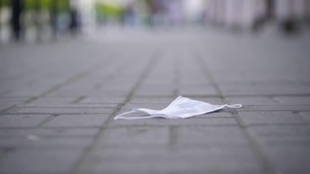 På trottoaren finns en använd skyddsmask. Sådant skräp medför en biologisk fara för andra. — Stockvideo