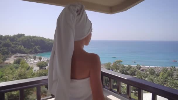 Een mooie, slanke vrouw kijkt uit op het balkon van een elite hotel. Een jonge vrouw na het douchen in een handdoek. — Stockvideo
