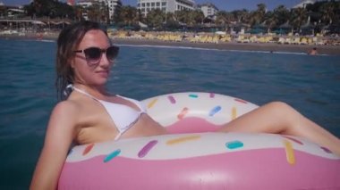 Bekini 'de güzel bir kadın denizde dinleniyor. Güneş gözlüklü genç bir kadın şişirilebilir bir dairede yüzüyor..