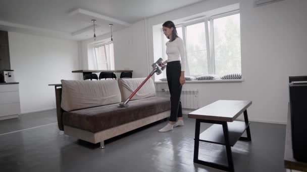 Een moderne draadloze stofzuiger. Handmatig reinigen in een grote woonkamer, brunette meisje. — Stockvideo