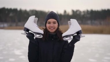 Koyu renk ceketli genç bir kadın buz pateni yapmaya donmuş göle geldi. Kışın doğa eğlenceli olabilir..