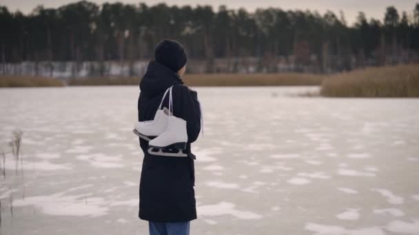 En ung kvinna i mörk jacka kom till den frusna sjön för att åka skridskor. På vintern kan naturen vara rolig. — Stockvideo