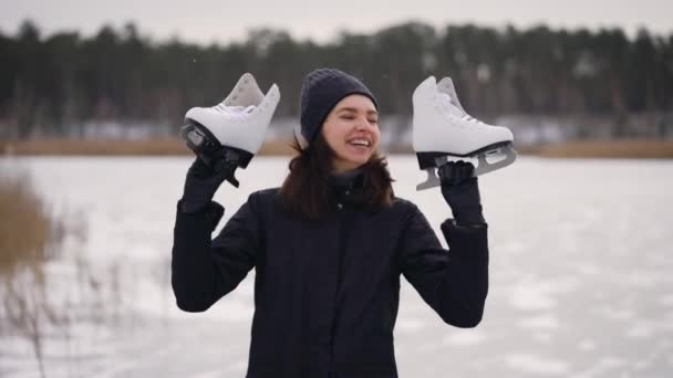 Una joven con una chaqueta oscura, llegó al lago helado para ir a patinar sobre hielo. En invierno, la naturaleza puede ser divertida. — Vídeos de Stock