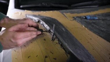 Ellerinde halkalar olan bir usta bir parçanın şeklini gösterir. Bir adam spor kaputunun maketi üzerinde çalışıyor. Akort atölyesi