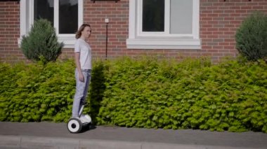 İnce, genç bir kız şehir caddesi boyunca jiroskoplu scooter kullanıyor. Modern elektrik taşımacılığı.