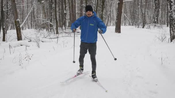 En ung man är engagerad i längdskidåkning i vinterskogen. Idrottaren springer skridskor. — Stockvideo