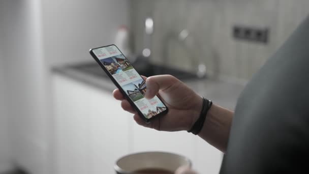 Un hombre elige un nuevo hogar para sí mismo a través de una aplicación en un teléfono inteligente. Selección remota y compra de bienes raíces desde el teléfono. — Vídeo de stock