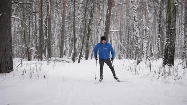 Un joven se dedica al esquí de fondo en el bosque invernal. El atleta corre patinaje. — Vídeos de Stock