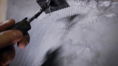 Heykeltıraş, çalışma stüdyosunda plastik kazıyıcı kullanarak siyah plastiksi endüstriyel örnek kazıyor.