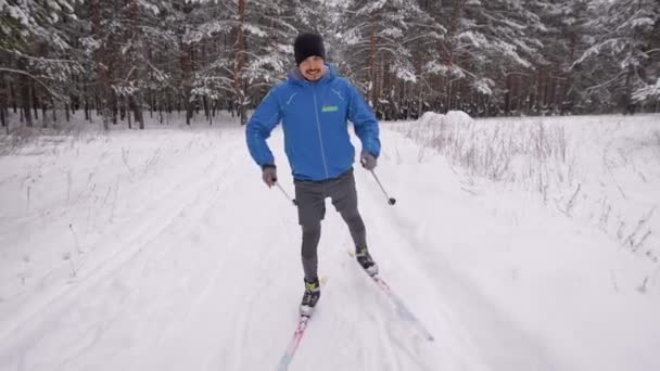 Un joven se dedica al esquí de fondo en el bosque invernal. El atleta corre patinaje. — Vídeos de Stock