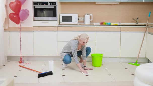 Eine junge, schöne Blondine putzt die Küche. Die Frau ist müde und wartet auf das Ende der Reinigung. — Stockvideo